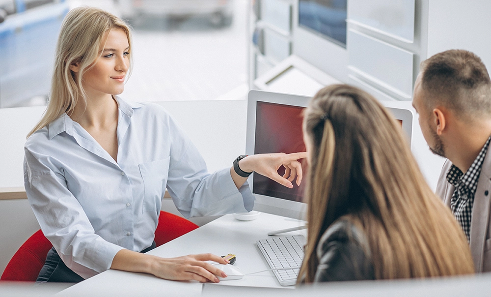 Immagine tematica di impiegata CIIP che illustra a due clienti informazioni sulle tariffe riportate sul monitor del suo computer