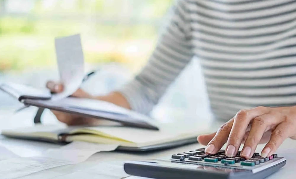 Immagine tematica con tavolo di lavoro in cui una donna analizza con la sua calcolatrice dei documenti contabili