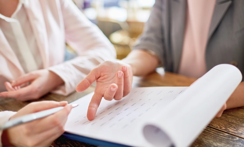 Immagine tematica con tavolo di lavoro in cui due impiegate lavorano su documenti contabili